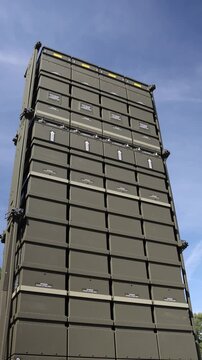 Vertical screen Patriot air defense missile launcher stands upright with four columns of missile canisters forming a massive vertical structure against the clear blue sky