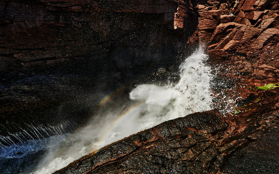  Thunder Hole in Acadia National Park, Maine, featuring a rainbow catching the mist of a crashing wave against the pink granite rock inlet, New England