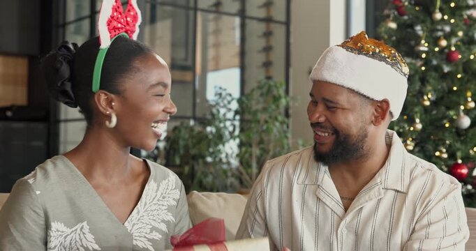 Christmas, present and black couple hug on home sofa for bonding, quality time and gratitude. Happy man, woman or festive season in house with kiss, xmas gift and surprise for holiday celebration