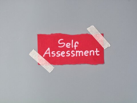 Self assessment handwritten note taped on grey background. Concept of personal growth, business evaluation, analysis, performance review, skill test, career development, and self improvement