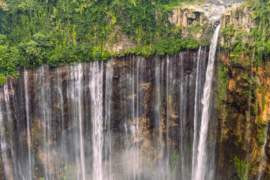 Tumpak Sewu Waterfall in Lumajang, East Java, Indonesia. Hundreds of cascading streams fall from a curved cliff into a lush tropical gorge, surrounded by dense rainforest and rising mist.