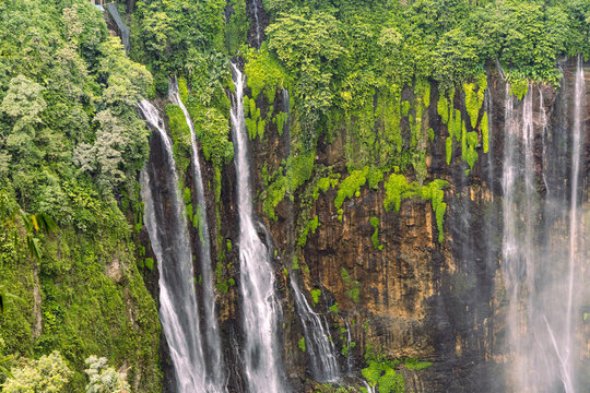 Tumpak Sewu Waterfall in Lumajang, East Java, Indonesia. Hundreds of cascading streams fall from a curved cliff into a lush tropical gorge, surrounded by dense rainforest and rising mist.