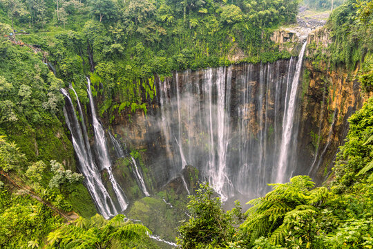Tumpak Sewu Waterfall in Lumajang, East Java, Indonesia. Hundreds of cascading streams fall from a curved cliff into a lush tropical gorge, surrounded by dense rainforest and rising mist.