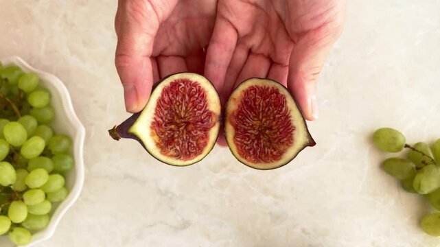 The woman opens and shows a fresh fig, top view. Fruit cut, preparing fruit for a work snack, healthy eating habits during a busy workday