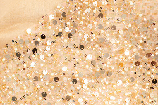 Gold sequin fabric with scattered shimmering sparkles on mesh textile