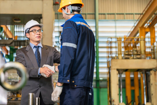 Industrial manager in suit handshaking with factory technician inside manufacturing plant, Asian business executive shaking hands with industrial engineer in heavy industry factory