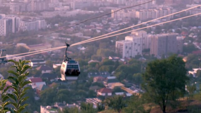 Kok Tobe cable car moving over Almaty city with residential buildings and green trees in Kazakhstan