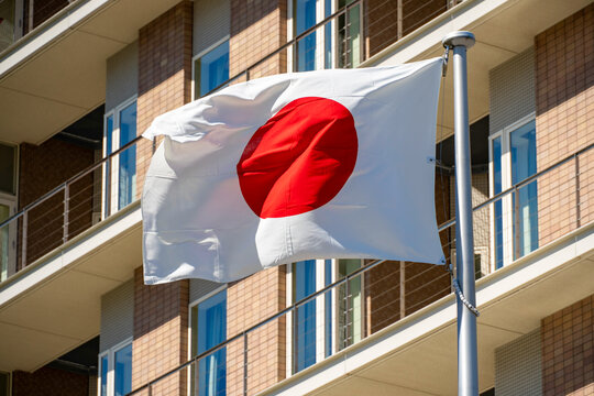 Japanese national flag fluttering dynamically under a clear sky with a stylish building behind
