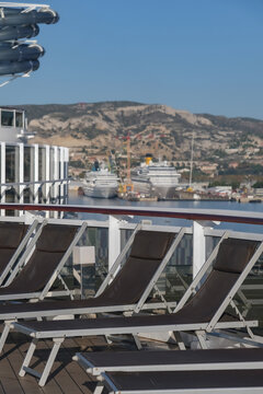 Pooldeck or swimmingpool with sun deck on modern cruiseship cruise ship liner in port with sun loungers ready for cruising to Mediterranean on sunny day with city skyline in background
