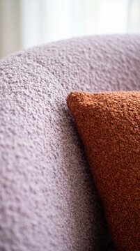 Textured lilac boucle sofa detail with rust cushion, soft window light and plush woven fabric
