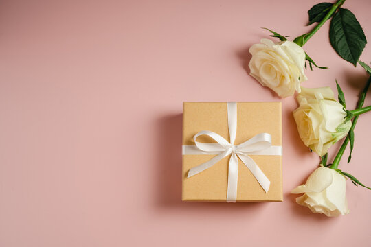 Gift box with white satin ribbon and cream roses on pink background
