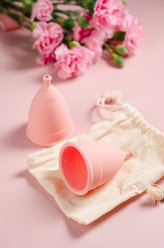 Reusable menstrual cups with cotton storage pouch and pink carnations on pink background