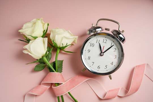 Menopause awareness concept with white roses and alarm clock on pink background