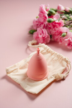 Reusable menstrual cup with cotton storage pouch and pink carnations on pink background