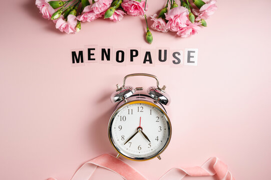 Menopause awareness concept with pink carnations and alarm clock on pastel background