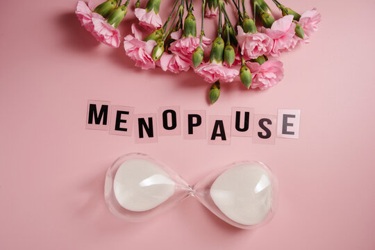 Menopause concept with hourglass and pink carnations on pastel background
