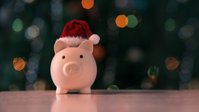 Piggy bank in Santa hat on Christmas tree background with bokeh. Concept of holiday spending, savings, budget, and financial planning. copy space