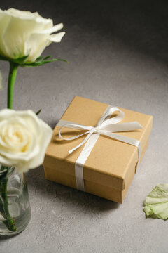 Kraft gift box with white satin ribbon and cream roses on textured background