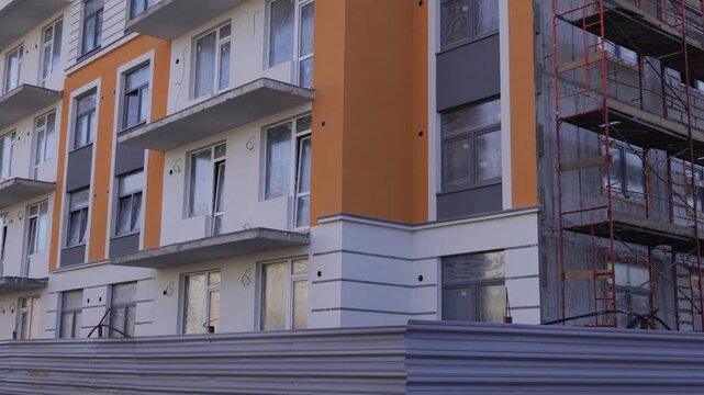 Modern multi-unit residential building under construction features white and orange facades, numerous window openings, and balconies