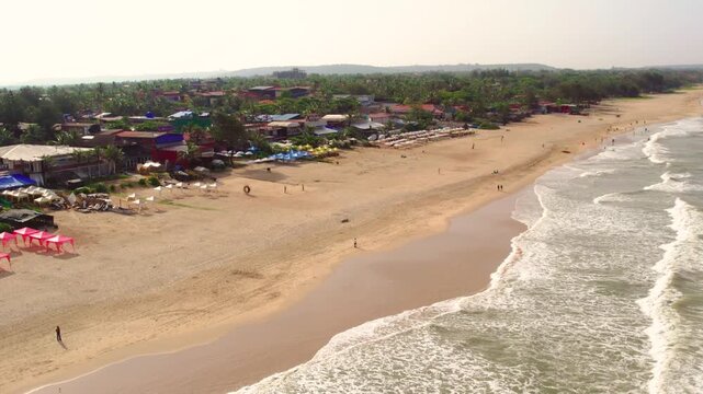 Aerial view of Vagator Beach with golden sand, gentle waves, and coastal buildings in Anjuna, Goa, India.