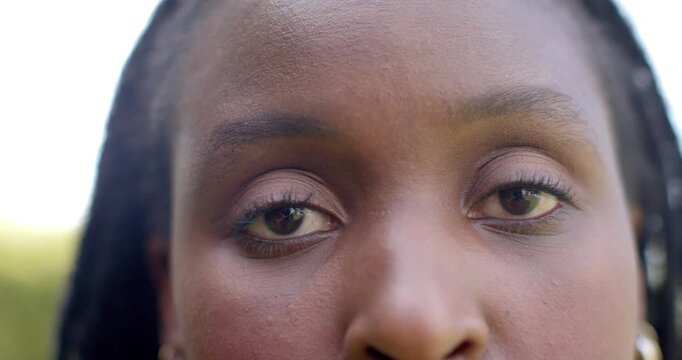 After direct gaze in bright light, woman with braids is shifting gaze downward, blinking to refocus