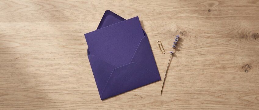 Flat lay of an open purple envelope with blank card, gold paperclip and dried lavender on a light wooden table &mdash; concept of elegant stationery symbolizing correspondence, invitations and thoughtful me