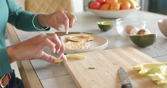 Person's hands are picking up avocado slices and placing on toast on marble top, making breakfast