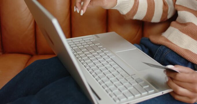 Hands are typing on laptop on brown sofa, holding card, finishing purchase, closing lid, resting