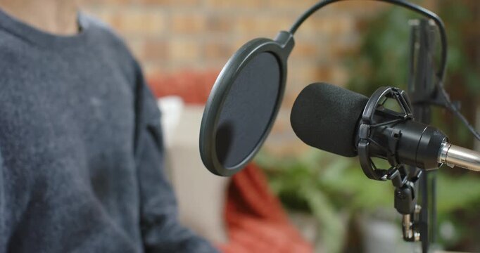 Starting to speak, seated speaker is gesturing right hand near mic pop filter during recording