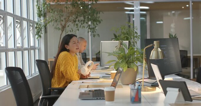 Diverse team listening after Asian woman showing white headset for input in office, copy space