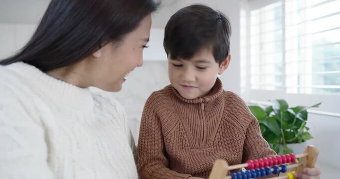 Diverse mother and son with mother pointing and son holding abacus and counting at table learning