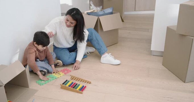 Diverse mother guiding son on floor, unpacking boxes, assembling foam puzzle and playing xylophone