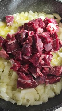 Trozos crudos de carne de ternera cortada en dados, colocada sobre una base de cebolla picada en una sart&eacute;n con aceite, para preparar estofado. Carrillada de ternera. 