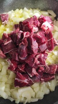   Trozos crudos de carne de ternera cortada en dados, colocada sobre una base de cebolla picada en una sart&eacute;n con aceite, para preparar estofado. Carrillada de ternera.