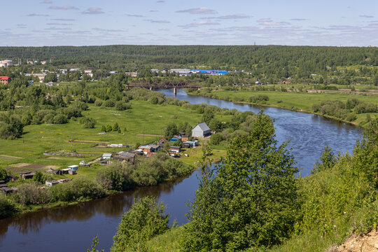 Boreal forest, river, green meadows, and private houses outside a provincial city in northern Russia.