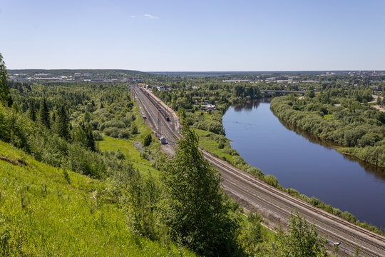 High angle view of railway and river flanked by green forest near a provincial city in northern Russia.