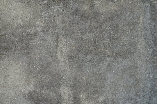 Grey concrete wall shows rough, weathered texture. Surface features subtle cracks and uneven grain patterns. Natural wear gives aged, industrial feel to the background. Suitable for construction
