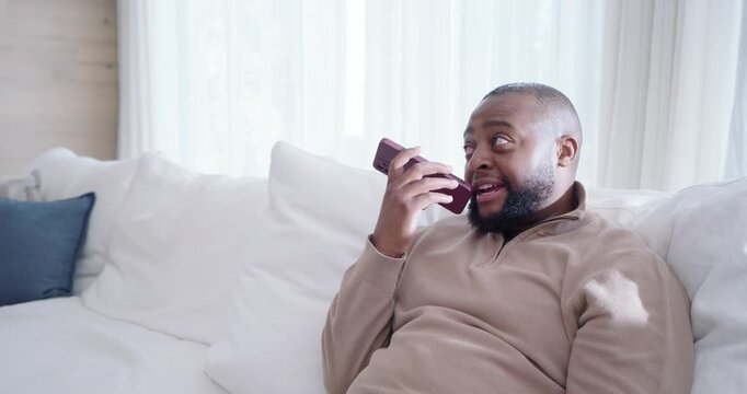 Receiving call, African American man speaking into phone, laughing, tapping screen on white sofa