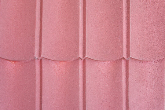 Close up of reddish pink ceramic roof tiles showing wavy pattern and rough texture. Construction material for house building exterior.