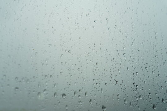 Water droplets on transparent glass surface with soft gray blue background. Rain drops pattern creating natural texture and abstract backdrop.