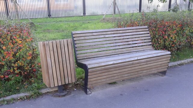 Modern wooden slat bench with black metal supports sits beside integrated wooden planter on paved edge