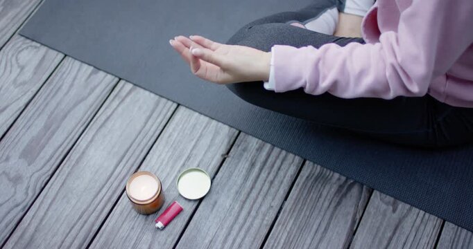 Woman in pink hoodie sitting on mat, camera panning, clapping to end practice, candle, copy space