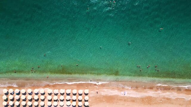 Top-down view of sandy beach with sun umbrellas and turquoise sea water