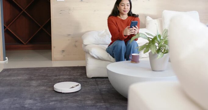 Robot vacuum starting to move, female sitting at home holding smartphone, reaching, guiding robot