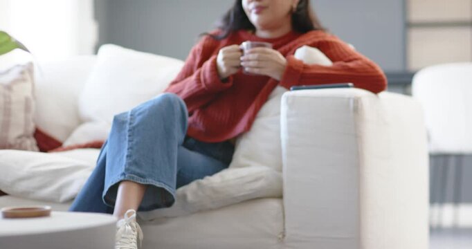 Robot vacuum moving across rug, camera pulling back, revealing woman sipping mug on sofa