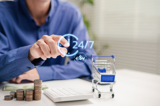 Professional touching a virtual 24/7 clock and currency exchange icon above stacked coins, a calculator and miniature shopping cart, illustrating online payments and nonstop financial services.