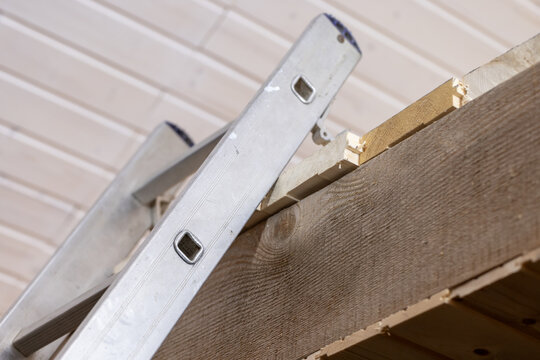 Aluminum ladder leaned against a wooden beam beneath a tongue-and-groove ceiling, showing a close-up view of home renovation, carpentry work, DIY repair and interior construction details