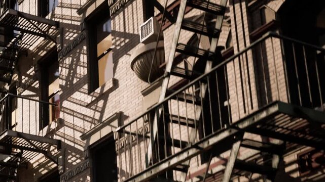Afternoon sun hits a brick building, casting fire escape shadows across the wall while light glows from within its arched windows.