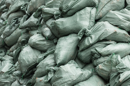 Stacked green woven sandbags tied and piled as a heavy-duty protective barrier for flood control and erosion prevention. Close-up view highlights texture, knots and used fabric