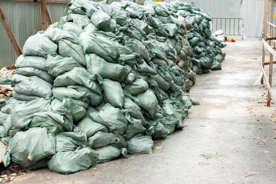 Large stacks of green sandbags line a pathway at a construction site, serving as a temporary flood barrier and protective measure against water, debris and erosion during storm or cleanup work